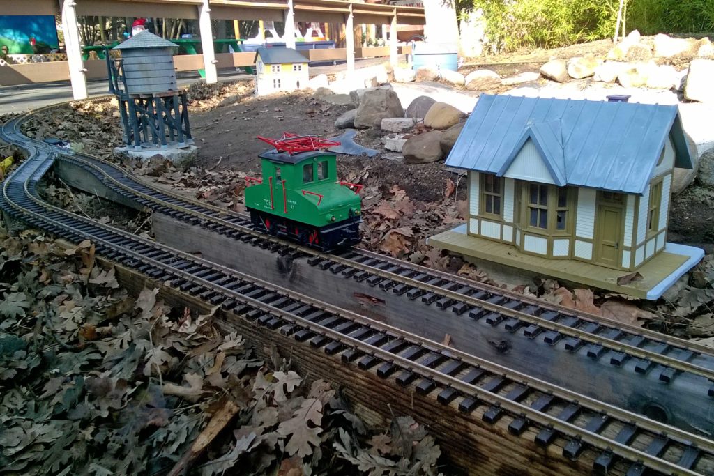 0-4-0 green locomotive model passes train station with water tank in background